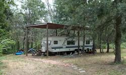 Beautiful, secluded, 9+ acres with new pipe fence along frontage. Build your dream home while you stay and play in the get-a-way spot provided. Covered deck,camper trailer stays,has a sturdy metal cover over it for protection. Water and electric already